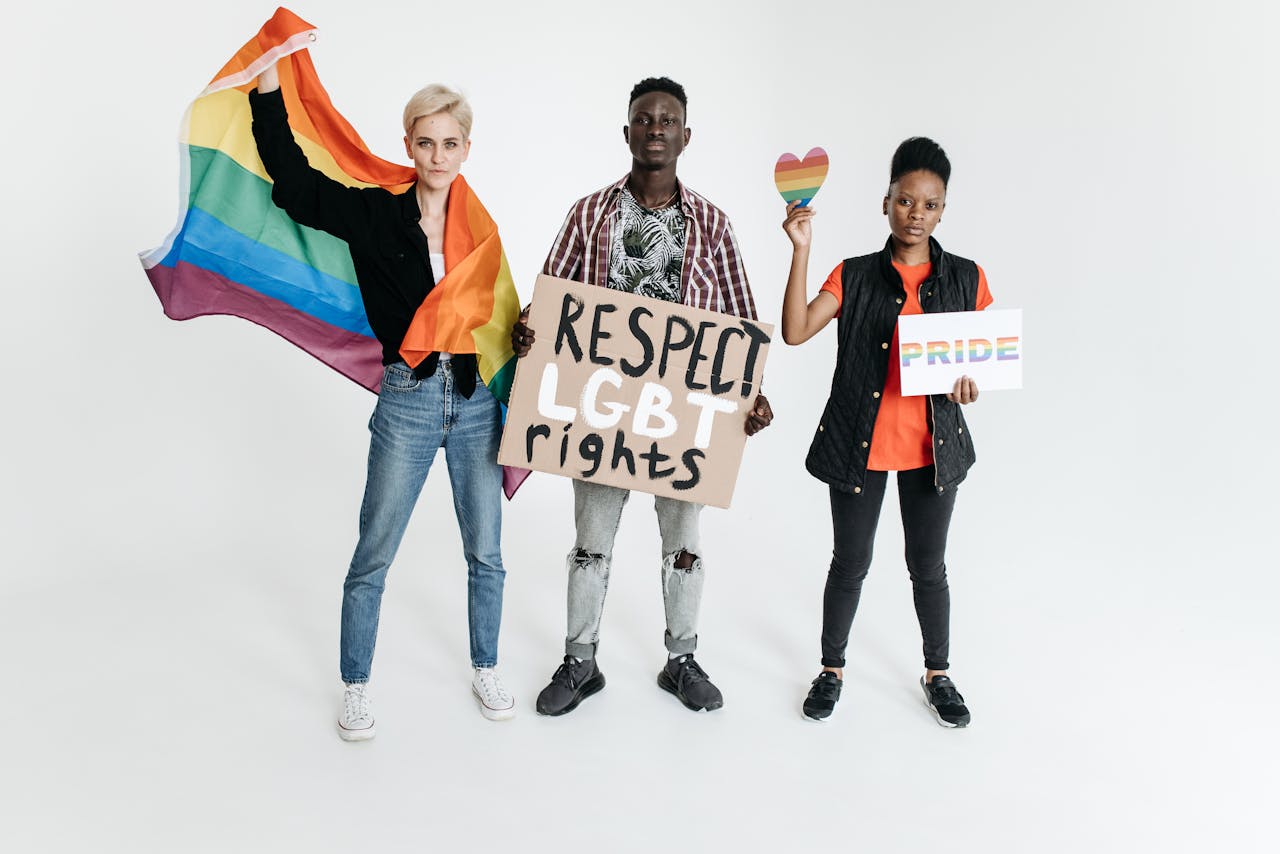 Three people holding pride signs advocating for LGBT rights with a rainbow flag.